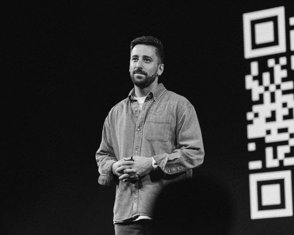 A speaker on stage next to a QR code on the screen
